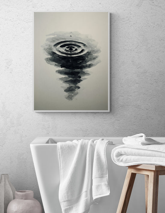 Tableau noir et blanc représentant une goutte d’eau créant des ondulations en style encre de Chine, accroché dans une salle de bain moderne avec baignoire blanche, serviettes pliées et tabouret en bois