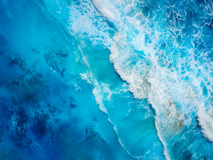 Aerial view of a turbulent sea, with white waves contrasting against the deep blue water. The detailed texture and vibrant hues create a sense of movement and freshness. Perfect for soothing and immersive wall decor.