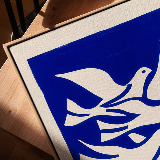 Klein blue canvas with white doves in oak frame displayed on a table