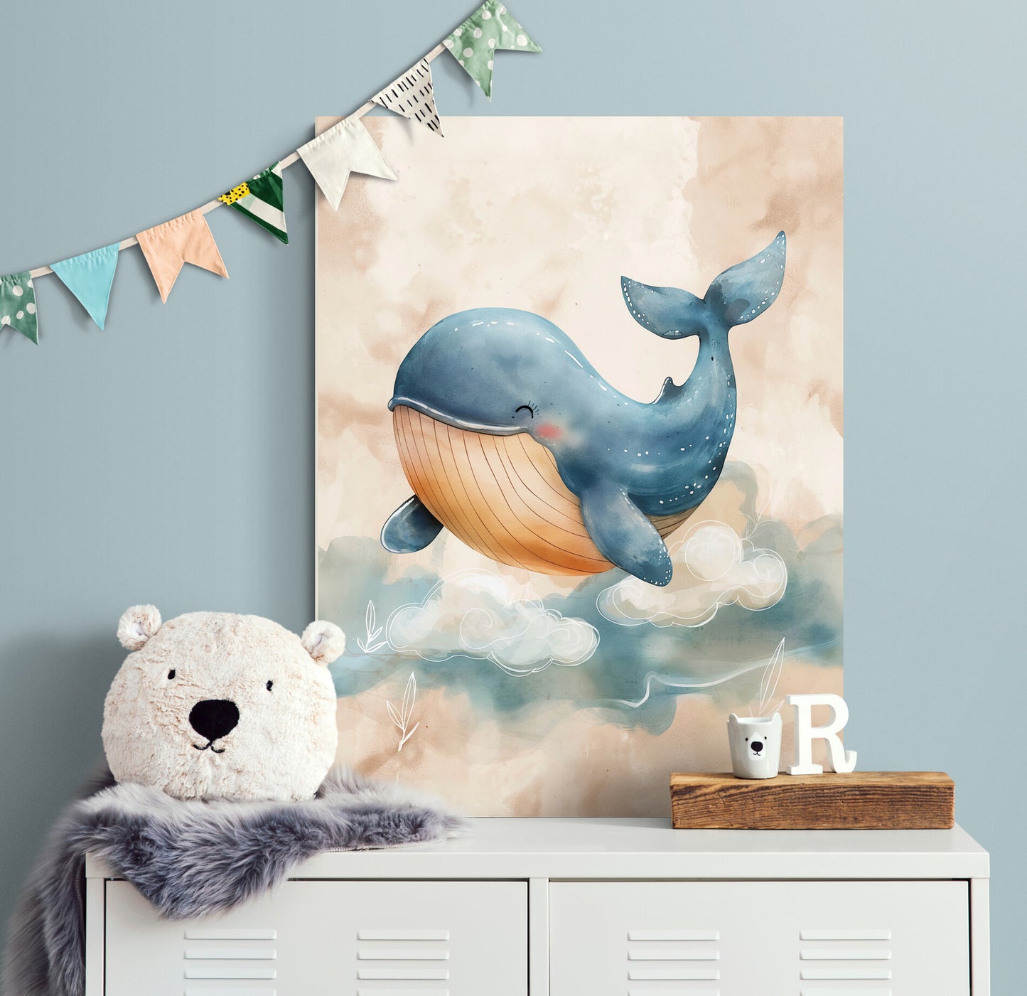 toile d'une baleine est affichée au-dessus d'un meuble blanc dans une chambre d'enfant, décorée de guirlandes colorées, avec un ours en peluche sur le meuble.