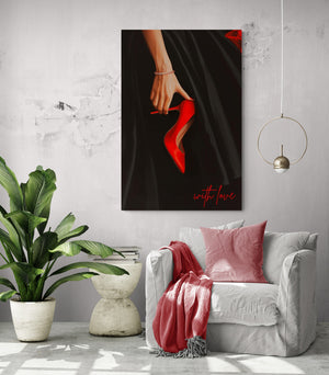 A white chair with a pink cushion and a pink blanket, next to a potted plant. Above the chair, a large artwork depicts a hand holding a red stiletto with the text "with love".