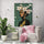 Frida Kahlo XXL wall art decor in a bright reading corner with a white chair, pink cushion, tropical plant, and a slightly textured white wall. Ideal for a zen space.