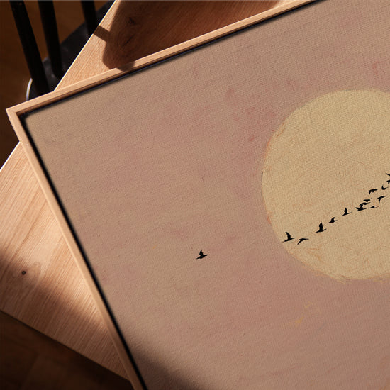 Blush pink moon and birds canvas with golden oak frame on a living room table, serene decor