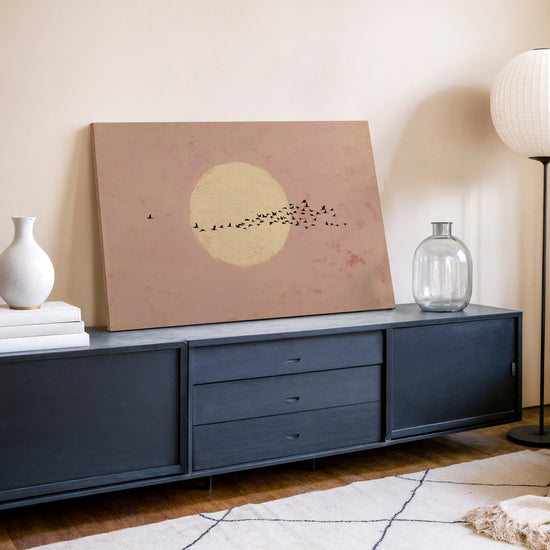 Zen birds in flight with a golden moon, blush pink canvas hung above a modern living room sideboard