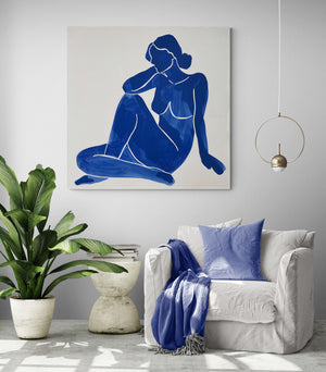 living space, comfortable armchair, dark blue cushion and plaid, modern side table, large green plant, woman painting