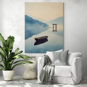 Grande toile murale japonaise représentant une barque solitaire flottant sur un lac calme face à un torii traditionnel, accrochée dans un salon moderne avec fauteuil blanc, coussin décoratif, plaid gris, plante verte tropicale et table basse en béton design