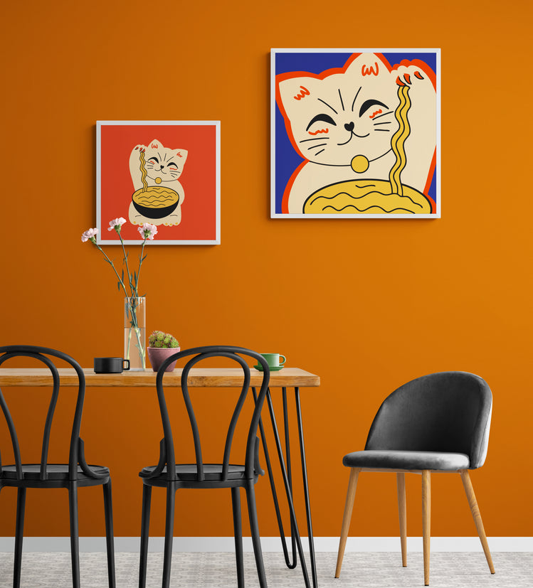 Dans une salle à manger les murs sont orange au centre une table et des chaises au style industriel. Accrochés au mur deux tableaux décorations murales de chat Maneki-neko sont accrochés au mur