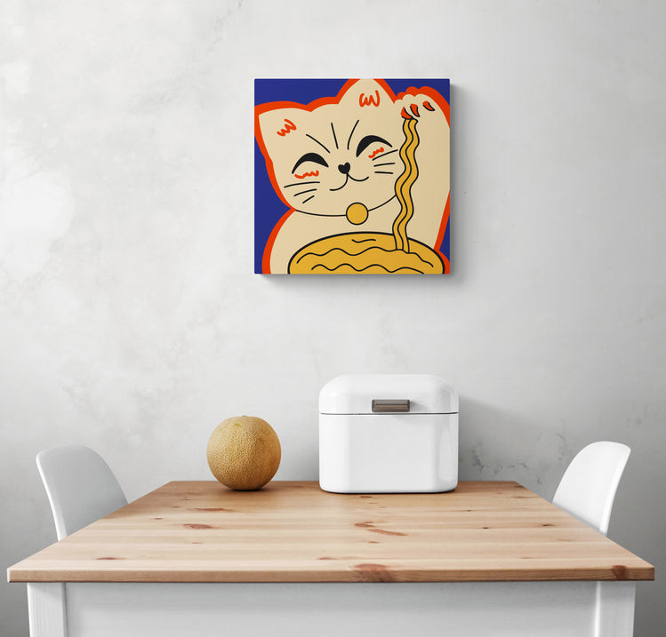 Tableau decoratif cuisine avec un chat maneki-neko est disposé au centre de l'image. Dessous une table de repas blanc et aux extrémités deux chaises blanche un melon et une boîte à pain sont sur la table.