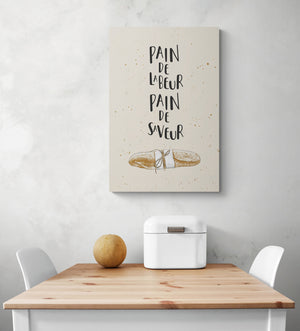 Tableau citation cuisine est suspendu au milieu d'une pièce blanche. Sur la photo sous le tableau se trouvent une table et deux chaises blanches.