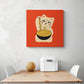 Un tableau orange avec un chat maneki-neko est disposé au centre de l'image. Dessous une table de repas blanc et en bois naturelle aux extrémités deux chaises blanche un melon et une boîte à pain sont sur la table.