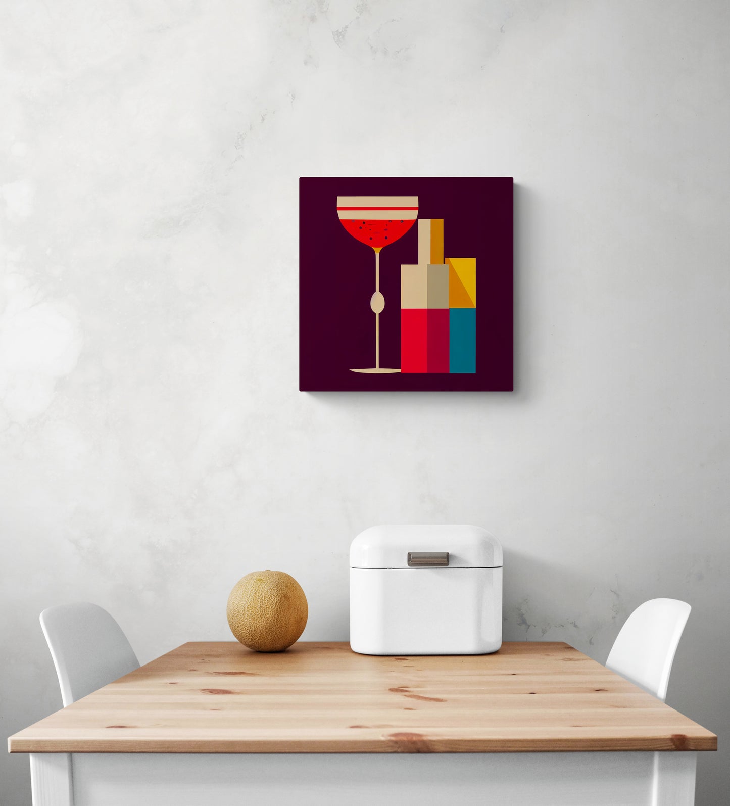 Un tableau toile cuisine en dessin à plat de couleurs chaudes avec une illustration graphique d'une bouteille et d'un verre de cocktail. Le tableau décoratif est accroché sur un mur blanc. Une corbeille à pain en métal blanc et un melon sont posés sur une table en bois. Deux chaises blanches sont aux extrémités de la table 
