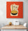 In a white kitchen, an orange decorative canvas featuring a Maneki-neko cat holding a black bowl of noodles is hung on the wall, with a table and two white chairs beneath it.