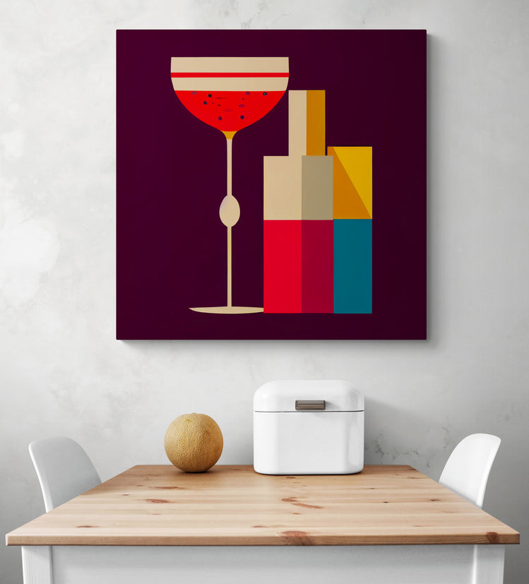 Un tableau pour cuisine en impression haute définition d'une illustration géométrique coloré d'une bouteille et d'un verre de cocktail. La toile murale est accrochée sur un mur blanc. Une corbeille à pain en métal blanc et un melon sont posés sur une table en bois. Deux chaises blanches sont de chaque cotée.