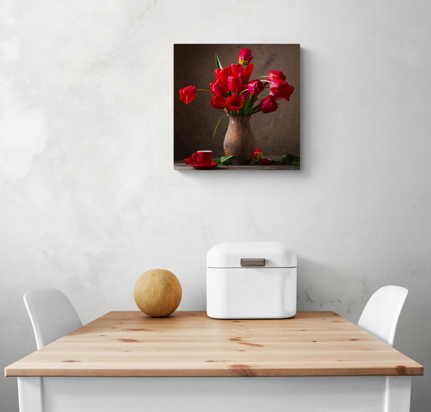 Un petit tableau deco pour cuisine avec des fleurs rouges est accroché sur un mur blanc au-dessus d'une table de cuisine en bois