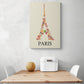 Sur un mur blanc d'une cuisine, un tableau aux couleurs douces représentant une image de la Tour Eiffel est accroché. La photo montre également une table en bois et deux chaises blanches qui semblent être disposées de manière à créer un espace accueillant.