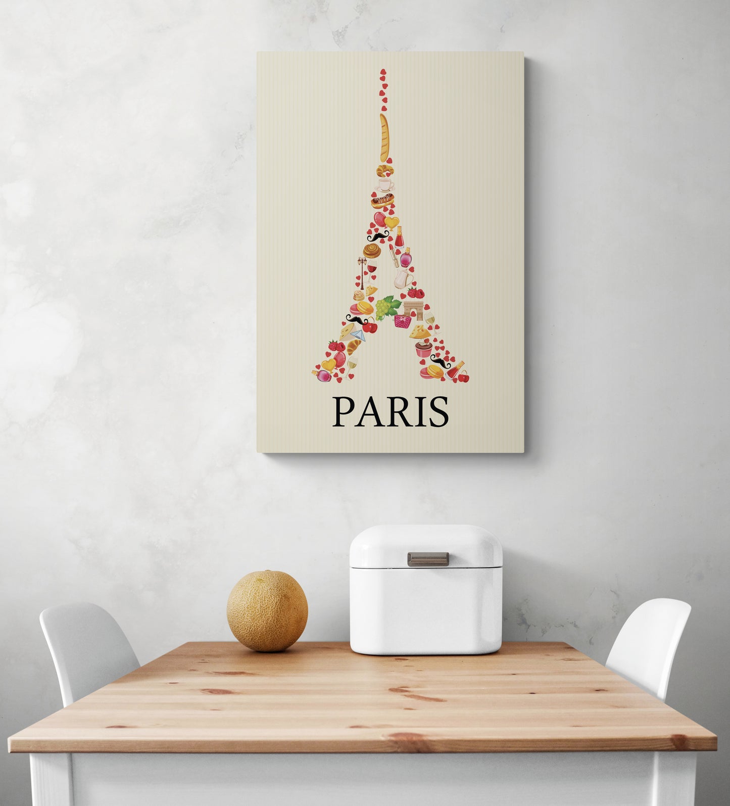 Sur un mur blanc d'une cuisine, un tableau aux couleurs douces représentant une image de la Tour Eiffel est accroché. La photo montre également une table en bois et deux chaises blanches qui semblent être disposées de manière à créer un espace accueillant.