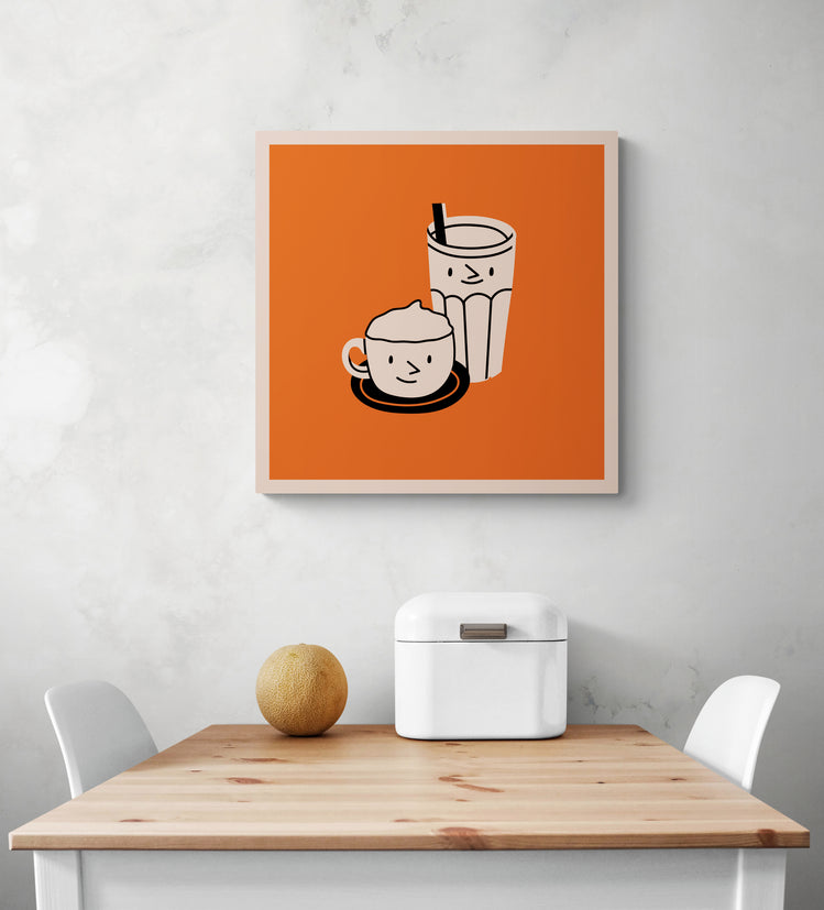 Un tableau deco pour cuisine orange est accroché sur le mur blanc. Ce tableau cuisine est placé au-dessus d'une table en bois et deux chaises sont de chaque côté. Une boîte à pain en métal blanc et un melon sont sur la table