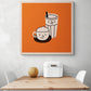 Un tableau orange est accroché sur le mur d'une cuisine blanche. Ce tableau cuisine est placé ce au-dessus d'une table en bois et deux chaises sont de chaque côté. Une boîte à pain en métal blanc et un melon sont sur la table