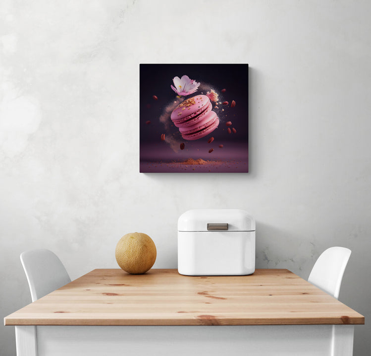 Une toile cadre au dessus d'une table de cuisine.Une photo sur toile de deux macarons roses flottant dans une explosion de saveurs, avec du sucre en poudre et du pollen doré autour. Une fleur de sakura ajoute une touche fleurie à cette gourmandise artisanale. Le focus est sur les formes douces des macarons et l'énergie de l'explosion en arrière-plan