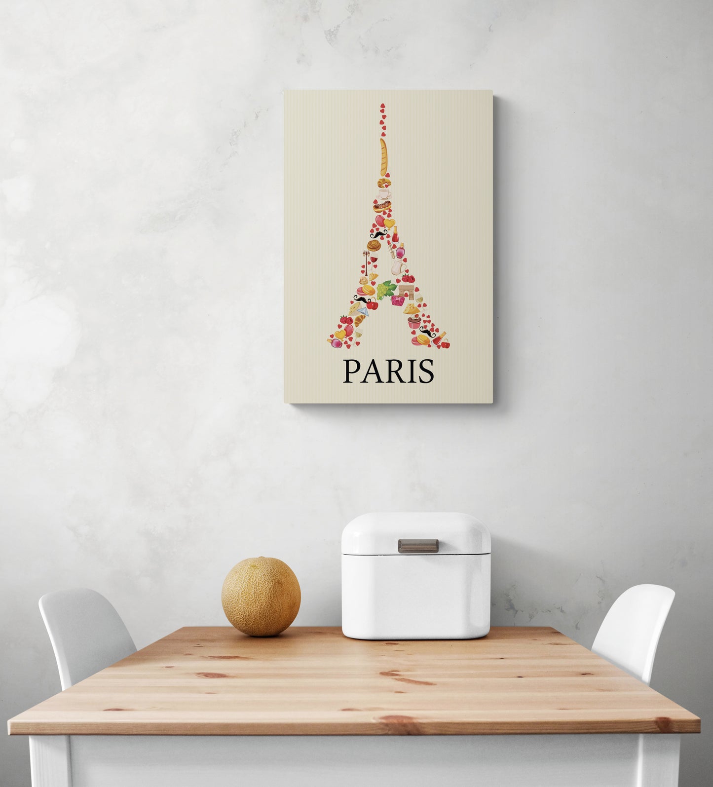 Sur un mur est accroché un tableau de la tour Eiffel, Les couleurs sont douces on peut voir des dessins de viennoiseries. La photo montre également une table en bois et deux chaises blanches qui semblent être disposées de manière à créer un espace accueillant.