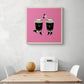 Un tableau deco pour cuisine rose est accroché sur le mur blanc. Ce tableau cuisine est placé au-dessus d'une table en bois et deux chaises sont de chaque côté. Une boîte à pain en métal blanc et un melon sont sur la table