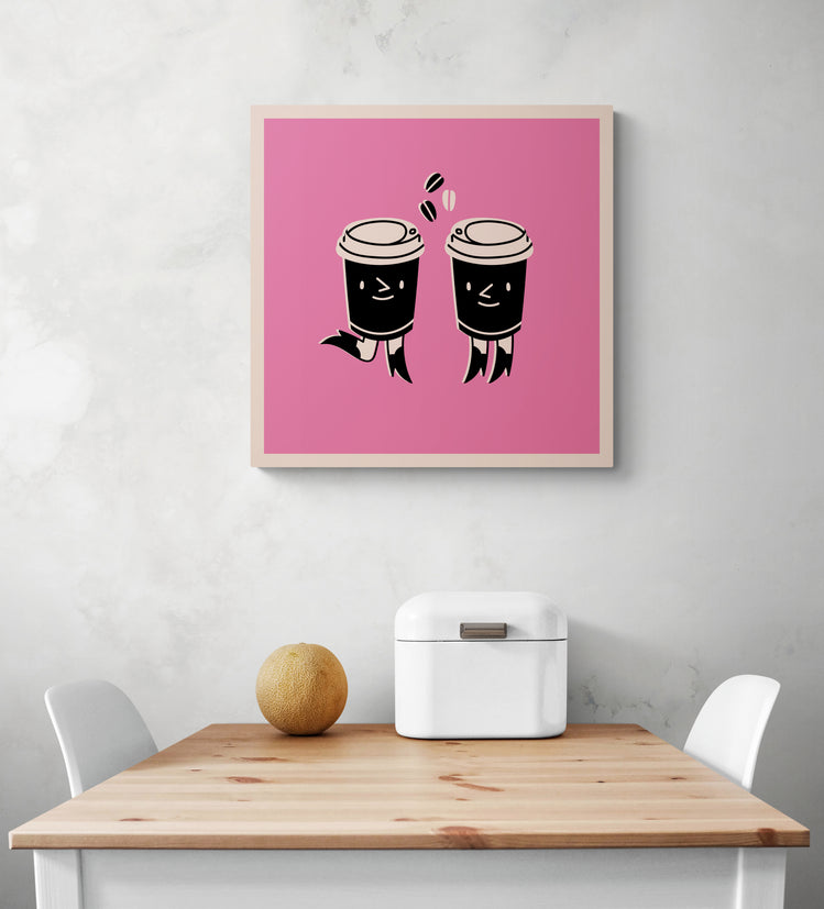 Un tableau deco pour cuisine rose est accroché sur le mur blanc. Ce tableau cuisine est placé au-dessus d'une table en bois et deux chaises sont de chaque côté. Une boîte à pain en métal blanc et un melon sont sur la table