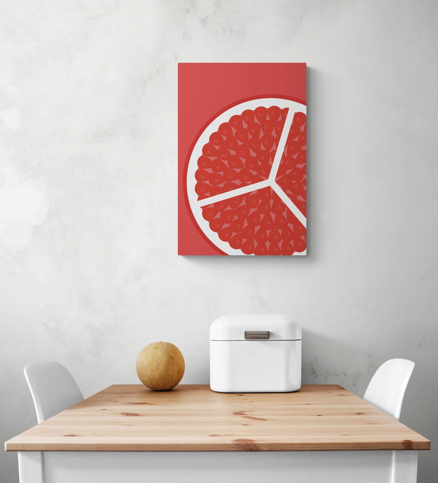 Un tableau mural cuisine est suspendu au centre d'un mur blanc. En dessous du tableau rouge se trouve une table et deux chaises blanche. Sur la table se trouve une boite à pain blanche et un petit melon vert.